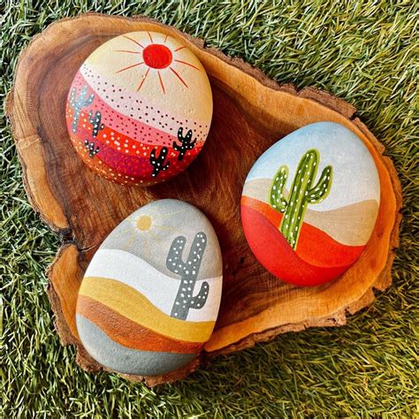 Two Painted Rocks Sitting On Top Of A Wooden Slice In The Grass Next To