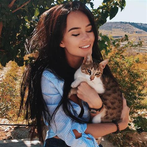 A Woman Holding A Cat In Her Arms And Smiling At The Camera With Hills