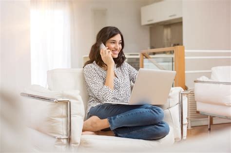 Mulher Jovem Sentada No Sofá Com Um Laptop E Falando Ao Telefone Em