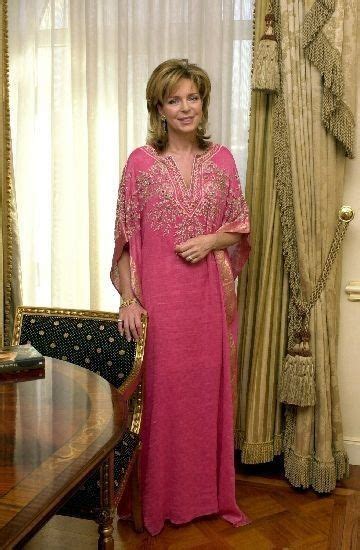 A Woman In A Pink Dress Standing Next To A Table And Curtained Window