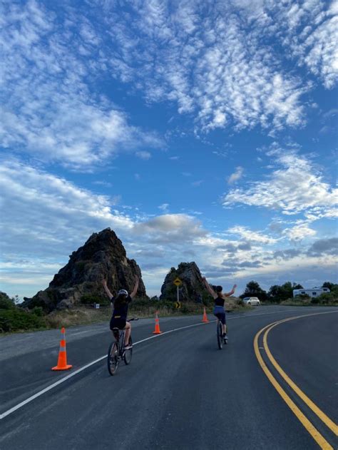 Two Bicyclists Are Riding Down The Road With Their Arms In The Air