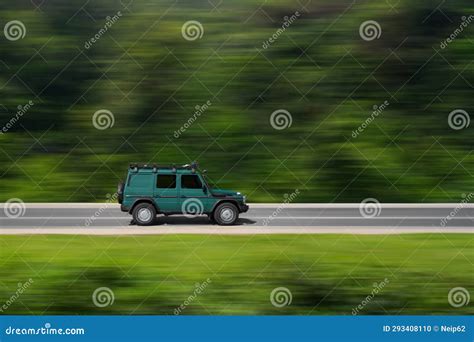 An Off Road Car Drives Along An Asphalt Road Through A Forest Side