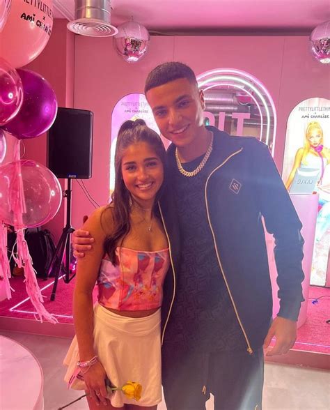 A Man And Woman Standing Next To Each Other In Front Of Pink Balloons