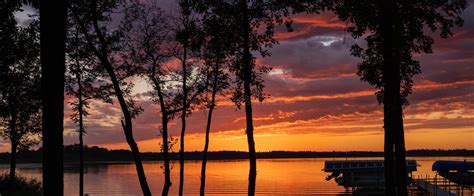 Sunset Over A Beautiful Lake Through Silhouette Of Trees And Boats