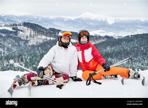 Two Friends Wearing Ski Suits And Ski Equipment Are In Winter Mountains