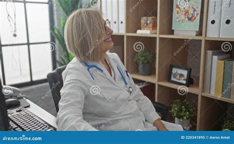 Mature Caucasian Female Doctor With Blonde Hair In Her Office Wearing A White Coat And