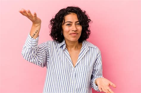 Jovem mulher latina encaracolada isolada em fundo rosa faz escala os braços sente se feliz