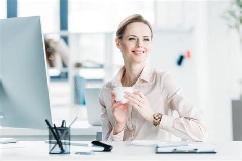 Smiling Businesswoman Drinking Coffee While Sitting At Office Stock