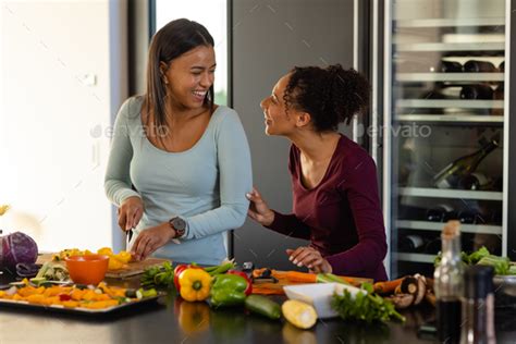 Happy Biracial Lesbian Couple Chopping Vegetables In Kitchen Stock
