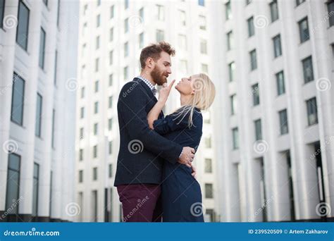 Man And Woman Hugging And Laughing In Front Of A White Building Stock