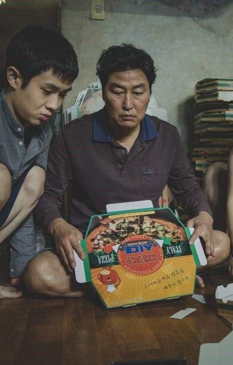 Two Men Sitting On The Floor Looking At A Pizza Box That Is In Front Of