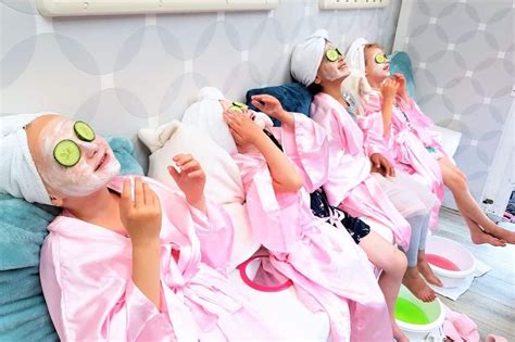 Several Women In Pink Robes With Cucumbers On Their Faces And One Woman