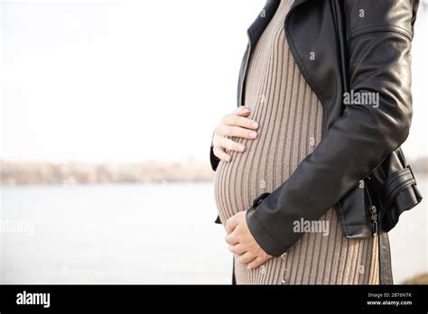 The Pregnant Woman In A Dress Holds Hands On A Stomach Pregnancy