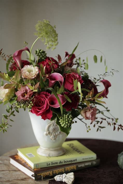 A White Vase Filled With Red And Pink Flowers On Top Of A Table Next To