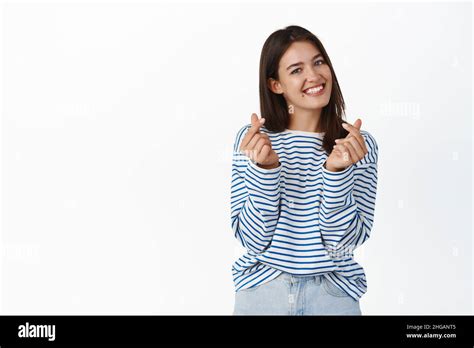 Cute Brunette Girl Smiling Showing Finger Hearts And Blushing Standing In Sweater Against