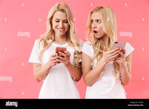 Beauty Blonde Twins Wearing In T Shirts Using Their Smartphones Over Pink Background Stock Photo