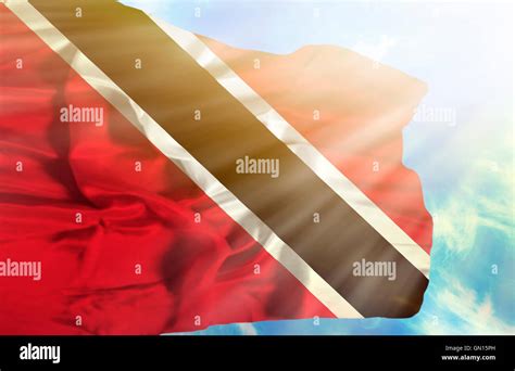 Trinidad And Tobago Waving Flag Against Blue Sky With Sunrays Stock