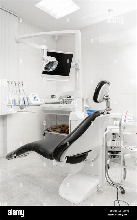 Vertical view of a dentist room with black seat. Modern dental practice. Dental chair and other ...