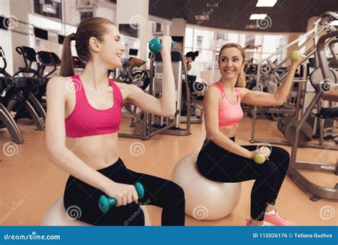 Two Women Sitting Doing Exercises With Dumbbells At The Gym They Look