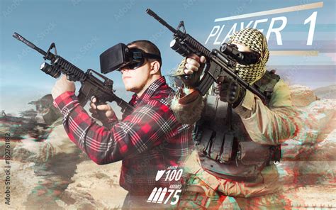 Vr gamer playing war game and aiming automatic rifle with fully equipped soldiers on desert ...