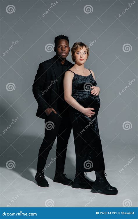 Young African Man And His Caucasian Pregnant Woman Stand Against Grey