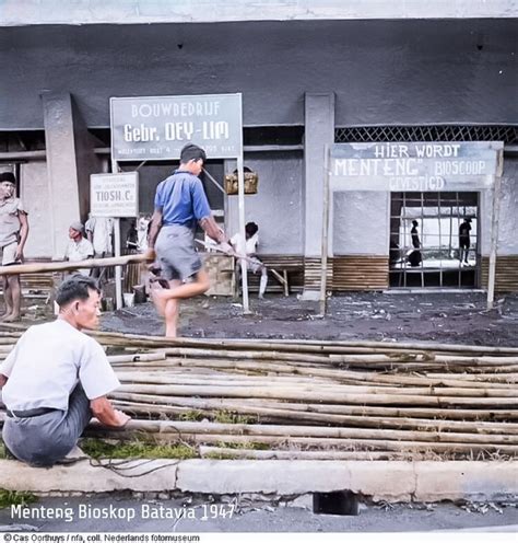 A Man Sitting On The Ground In Front Of A Building With People Standing