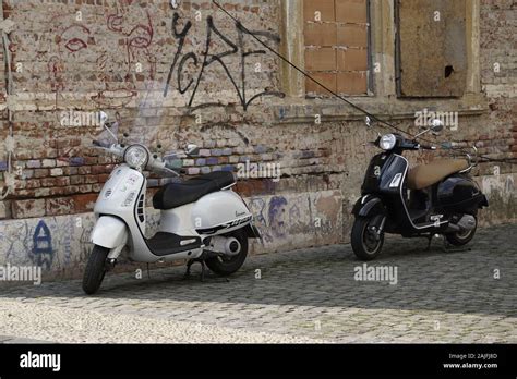 Two Old Fashioned Motor Scooters Parked On The Street Near A Brick Wall