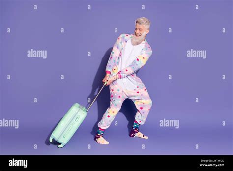 Joyful Mature Man In Star Patterned Unicorn Pajama Pulling Suitcase