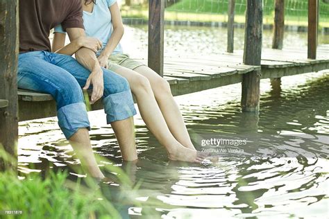 Couple Sitting On Dock Dangling Legs In Water Chest Down High Res Stock