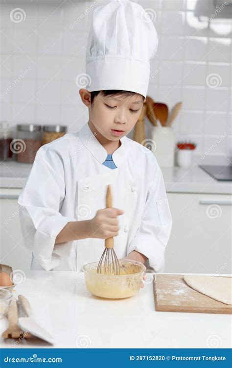 Happy Smiling Asian Boy In White Chef Uniform With Hat At Kitchen