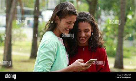 Candid Two Lesbian Women Kissing At Park Looking At Cellphone Stock