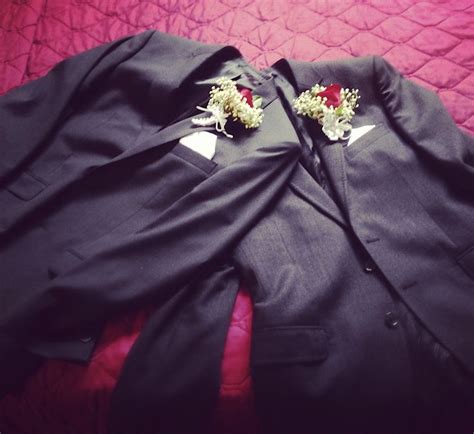 Two Black Suits With Red And White Flowers On Their Lapels Are Laying