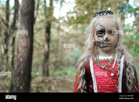 A child girl poses in a forest in a medieval dress in the image of a dead princess with makeup ...