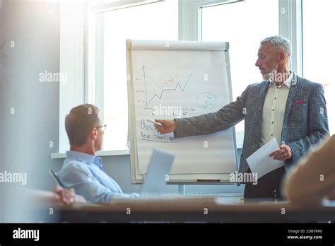 Confident Mature Businessman Pointing At Flip Chart And Explaining