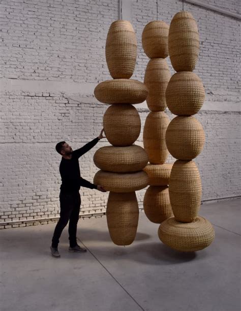 A Man Standing Next To A Tall Sculpture Made Out Of Woven Baskets On