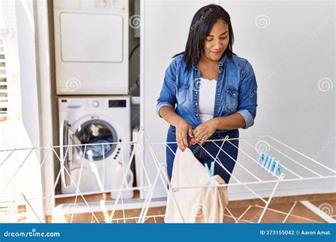 Hispanic Brunette Woman Hanging Clean Laundry On Rack At Laundry Room