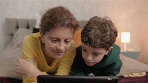 Mom And Son Watching Educational Video On The Tablet Lying On The Bed