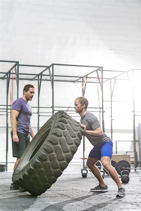 Man Looking At Dedicated Friend Flipping Tire In Crossfit Gym Stock