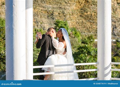 Young Beautiful Interracial Newlyweds Are Kissing In The Gazebo