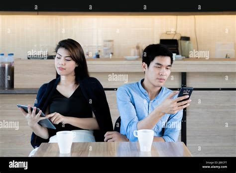 Asian Couple Looking At Their Mobile Phone While On A Date In Cafe Young Asian Couple Sitting