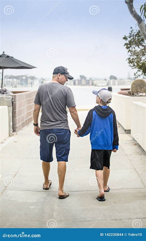 Father And Son Walking Hand In Hand Together On The Sidewalk Stock