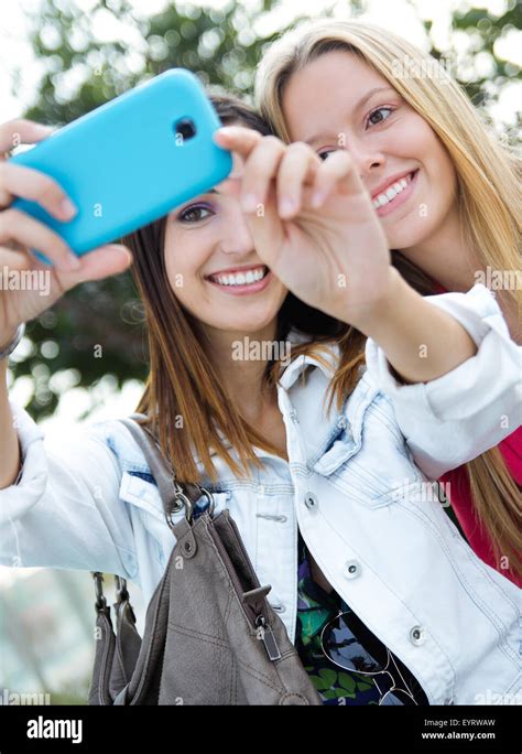 Outdoor Portrait Of Two Friends Taking Photos With A Smartphone Stock