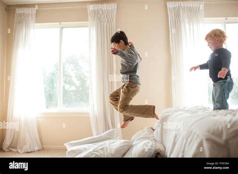 Brother having fun jumping off bed into pillows in bedroom Stock Photo - Alamy