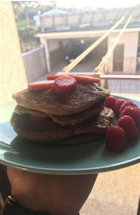 A Stack Of Pancakes With Raspberries On A Blue Plate In Front Of A Window