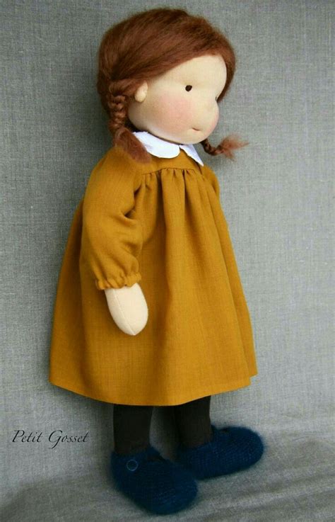 A Doll With Red Hair Wearing A Yellow Dress And Blue Slippers Is Posed