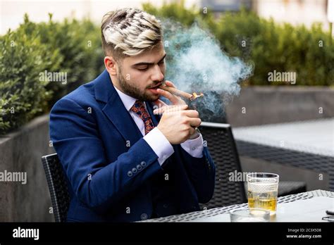 Stylish Handsome Man Smoking Cigar And Drinking Whiskey At A Cafe Stock