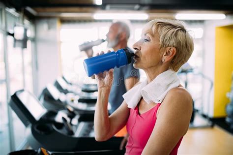 Senior Woman Drinking Bottle Of Water On Threadmill In Gym Stock Image