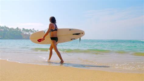 Woman Surfer In Bikini Holds Surfboard Walking Along Beach Stock