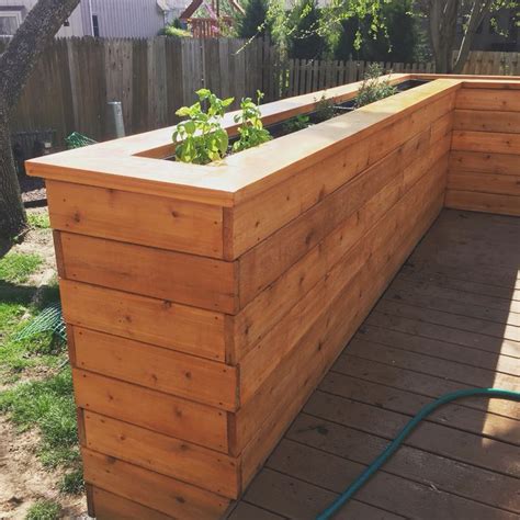 A Wooden Planter Box Sitting On Top Of A Wooden Deck Next To A Fence