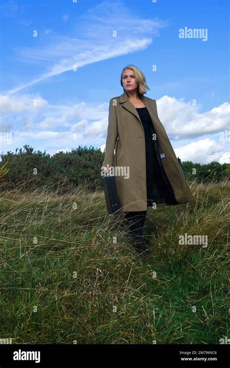 Blonde Woman In Long Green Coat Carrying A Briefcase In Grassland
